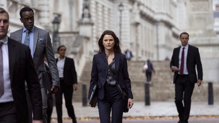 Netflix'teki The Diplomat'tan bir sahnede Kate, etrafı takım elbiseli başkalarıyla çevrili bir şekilde sokakta yürüyor.