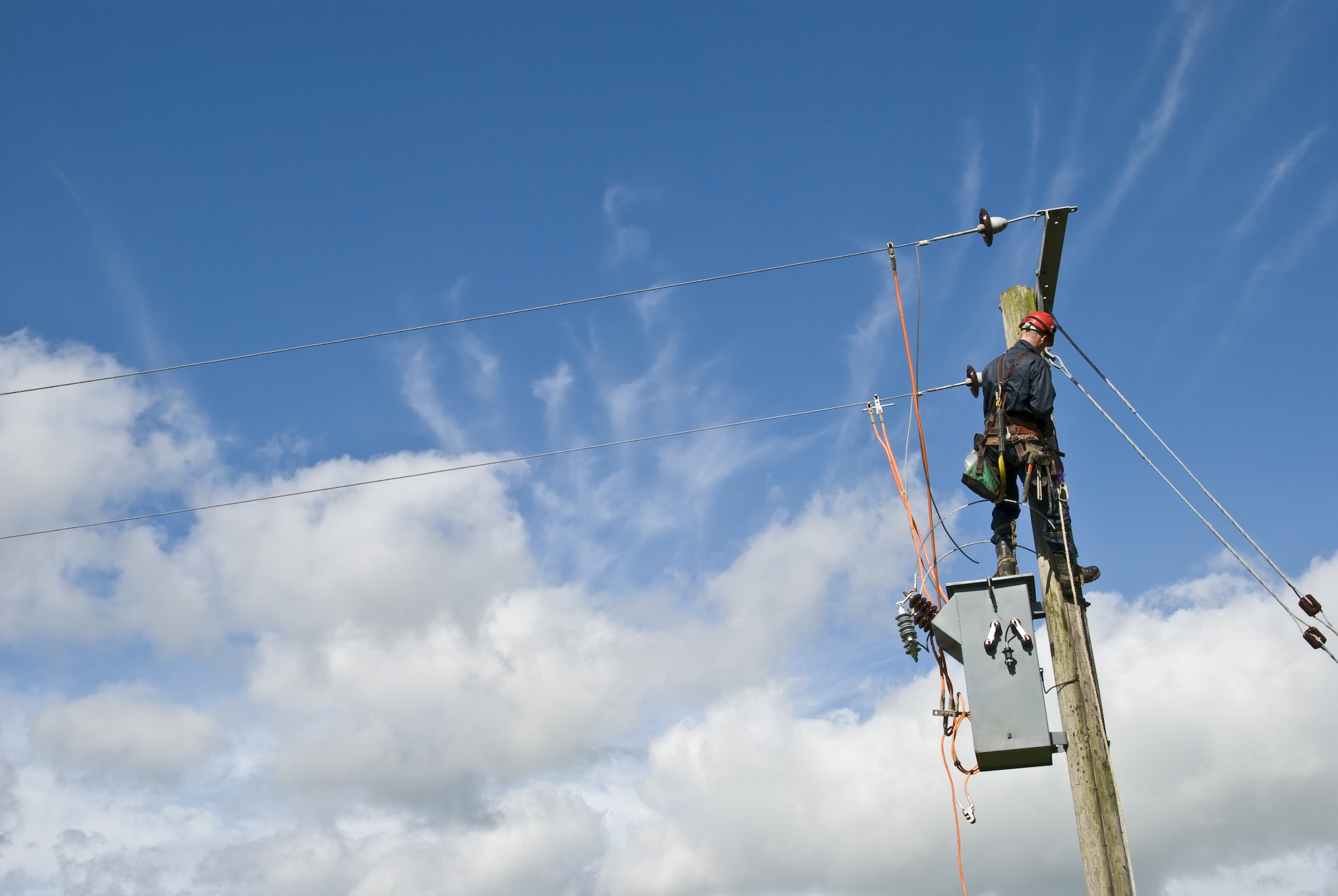 Mavi gökyüzünün altında elektrik hatlarını tamir eden kamu hizmeti çalışanı