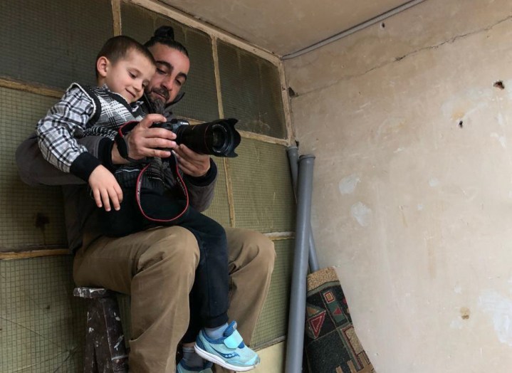 Bir fotoğrafçı kucağındaki bir çocuğa kamera gösteriyor.