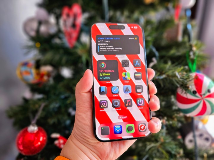 iPhone 15 Pro bir Noel ağacının önünde elinde tutuluyor.