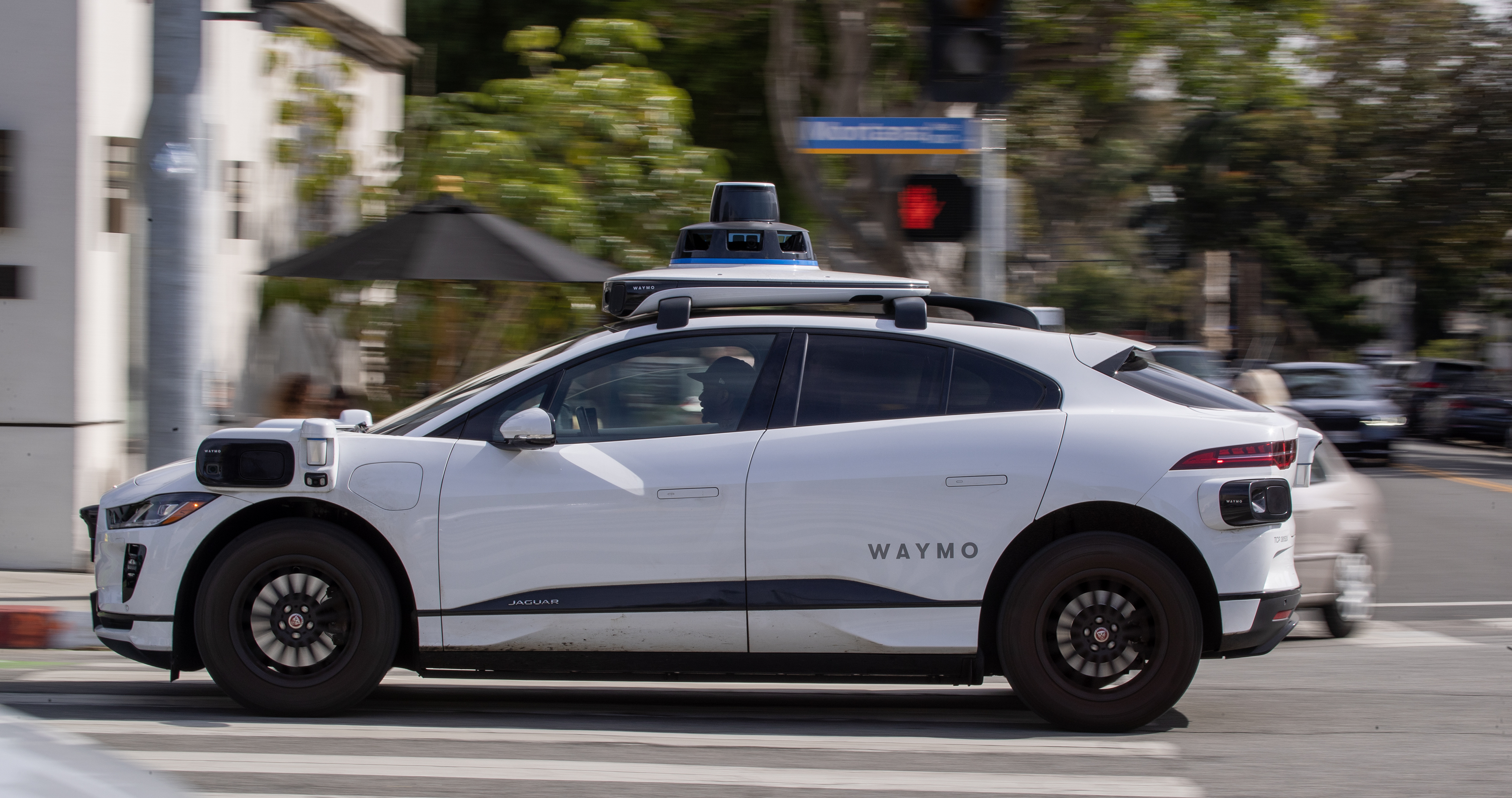 Santa Monica'da ağaçlarla çevrili bir caddede çalışan Waymo otonom aracı.