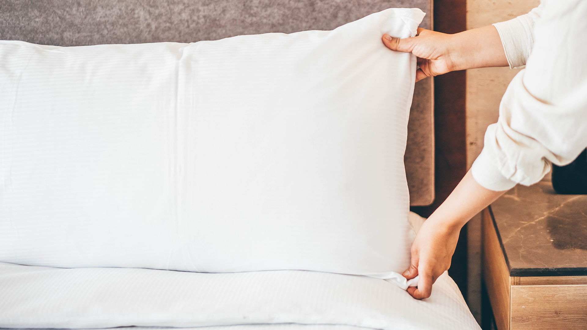 Bir çift el yeni temizlenmiş bir yastığı yatağın üzerine koyuyor