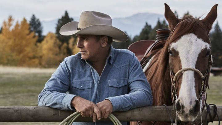 Kevin Costner Yellowstone'da bir atın yanında duruyor.