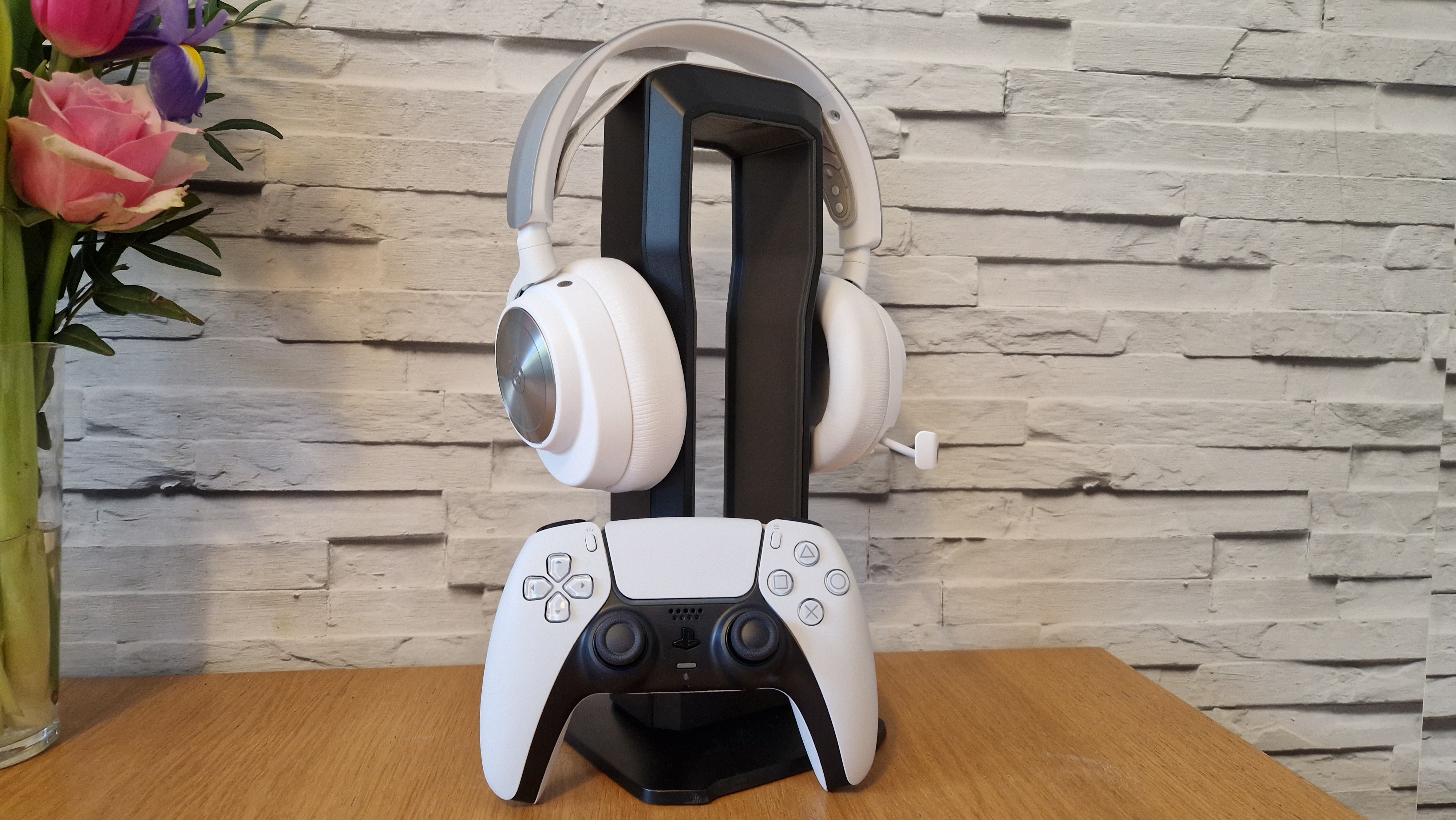 SteelSeries Arctis Nova Pro Wireless beyaz versiyonu, beyaz tuğla arka plana sahip bir kulaklık standı üzerinde
