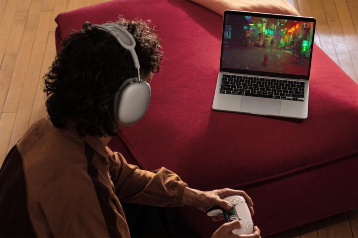 Bir kişi, gümüş renkli 13 inç MacBook Air'de PlayStation kumandasını kullanarak Stray oynuyor.