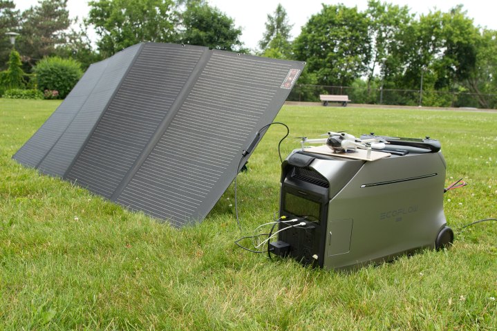 Güneş panellerine ve çeşitli kişisel cihazlara bağlı, çimenlerin üzerindeki EcoFlow Delta Pro 3 elektrik santrali.