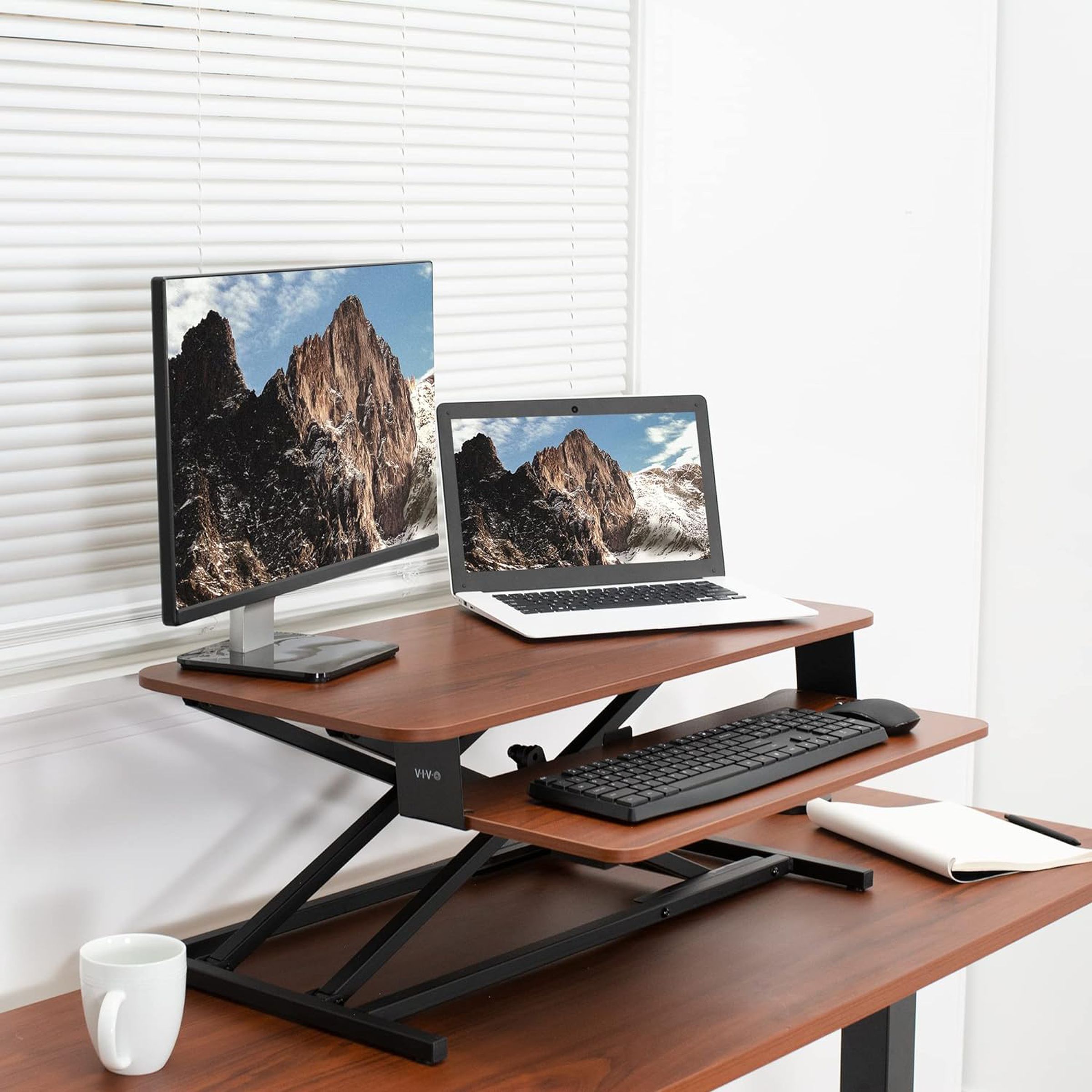 Bir masanın üstünde, monitör, dizüstü bilgisayar ve klavyeyi tutan iki katlı bir stand.