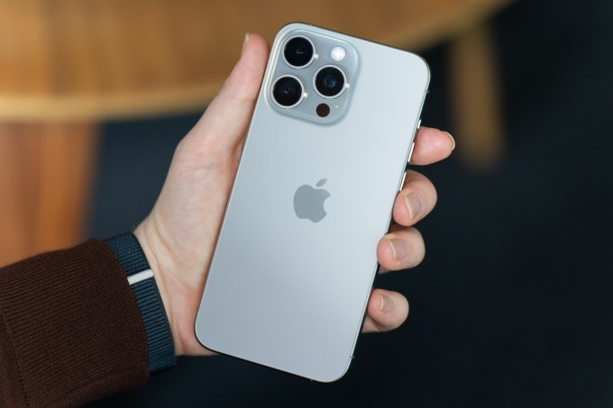 Doğal titanyumdan yapılmış iPhone 15 Pro Max, tutuluyor ve telefonun arkası gösteriliyor