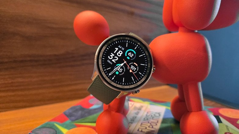 OnePlus Watch 2R masanın üstünde oyuncak bir köpeğe yaslanıyor