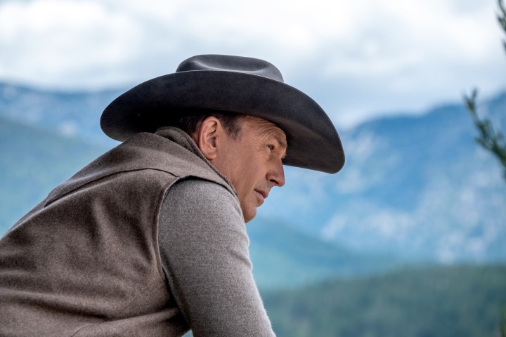 Kevin Costner Yellowstone'da bir çitin üzerinden eğiliyor.