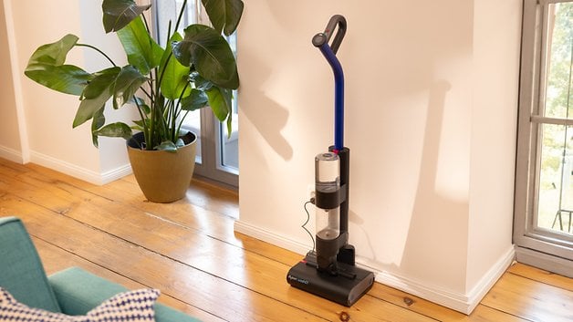 Dyson Wash G1, aydınlık bir odada büyük bir saksı bitkisinin yanındaki duvarın önünde duruyor.