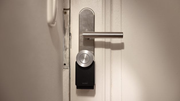 Gümüş kulplu ve kilit mekanizmalı bir kapının üzerinde Nuki Smart Lock Pro.