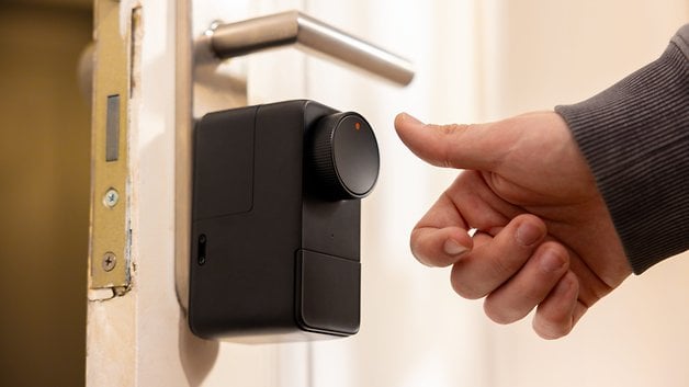 Bir el, bir düğme ve hafif kırmızı bir ışıkla gösterilen, kapının üzerinde SwitchBot Lock Pro'yu kullanıyor.