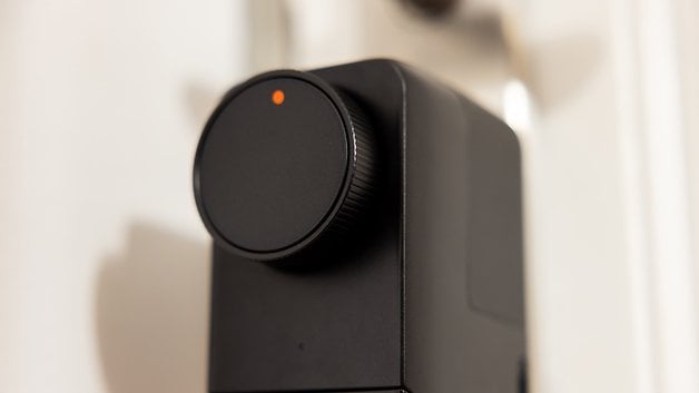 Yuvarlak düğmeli ve turuncu gösterge ışıklı SwitchBot Lock Pro cihazının yakından görünümü.