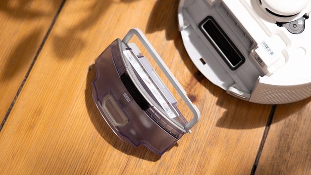 SwitchBot K10 Pro'nun ahşap zemin üzerinde cihazın yanındaki toz kutusunun yakından görünümü.