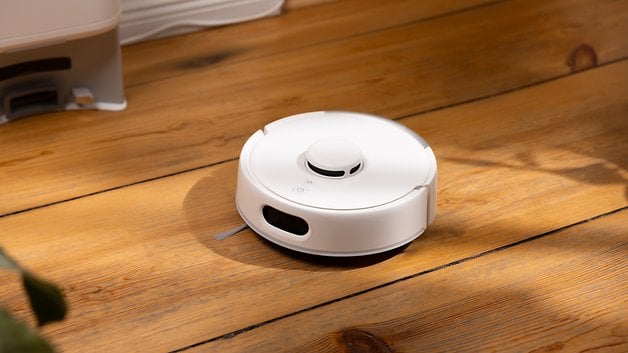 SwitchBot K10 Pro etiketli, ahşap zemin üzerinde beyaz bir robot elektrikli süpürge.