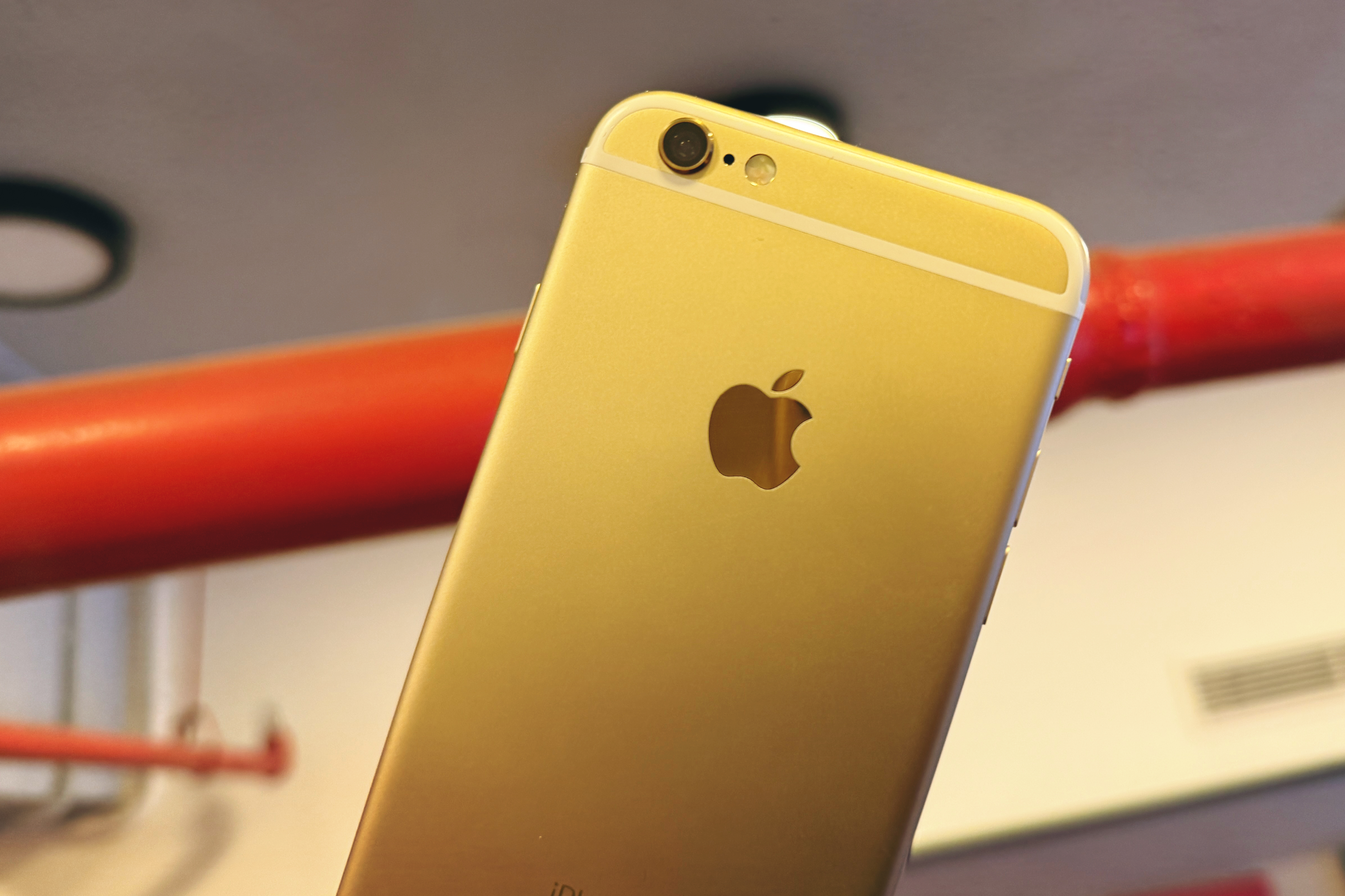 Kırmızı bir boruya yaslanmış altın renkli bir iPhone 6S.