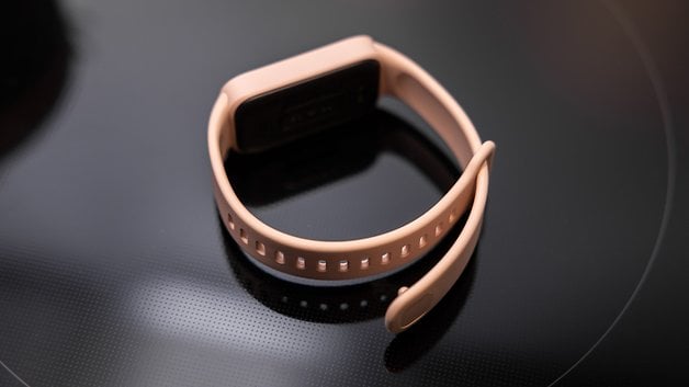 Xiaomi Smart Band 9 Active, siyah bir yüzey üzerinde yumuşak pembe renktedir.