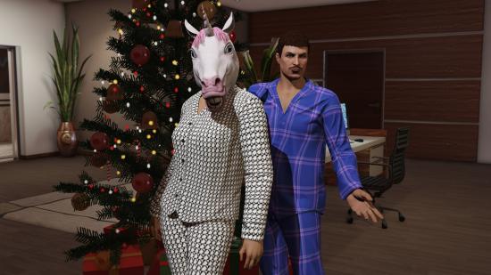 En iyi Noel oyunları - dev bir Noel ağacının olduğu bir ofiste duran pijamalı bir çift. Açık renk pijama giyen kadın da tek boynuzlu at maskesi takıyor.