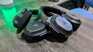 Yeşil aydınlatmalı bir masanın üzerinde birbirine yaslanmış iki Razer Barracuda X Chroma kulaklık.