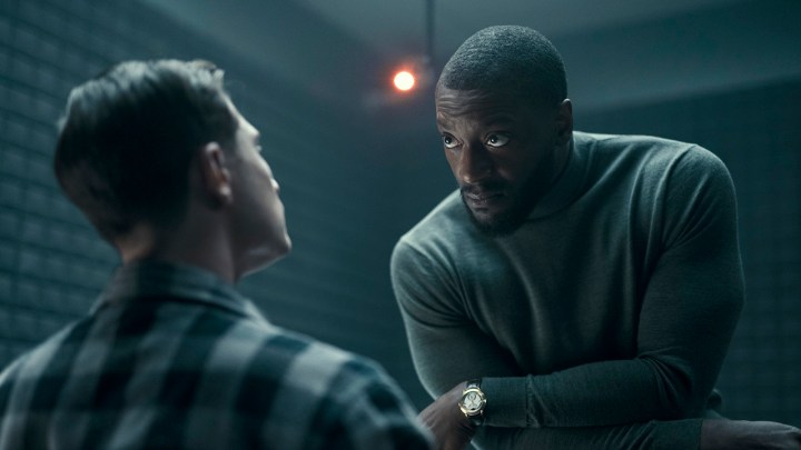 Alex Cross, Amazon Prime Video'daki Cross'tan bir sahnede bir masanın üzerinde oturmuş bir suçluyu sorguya çekiyor.