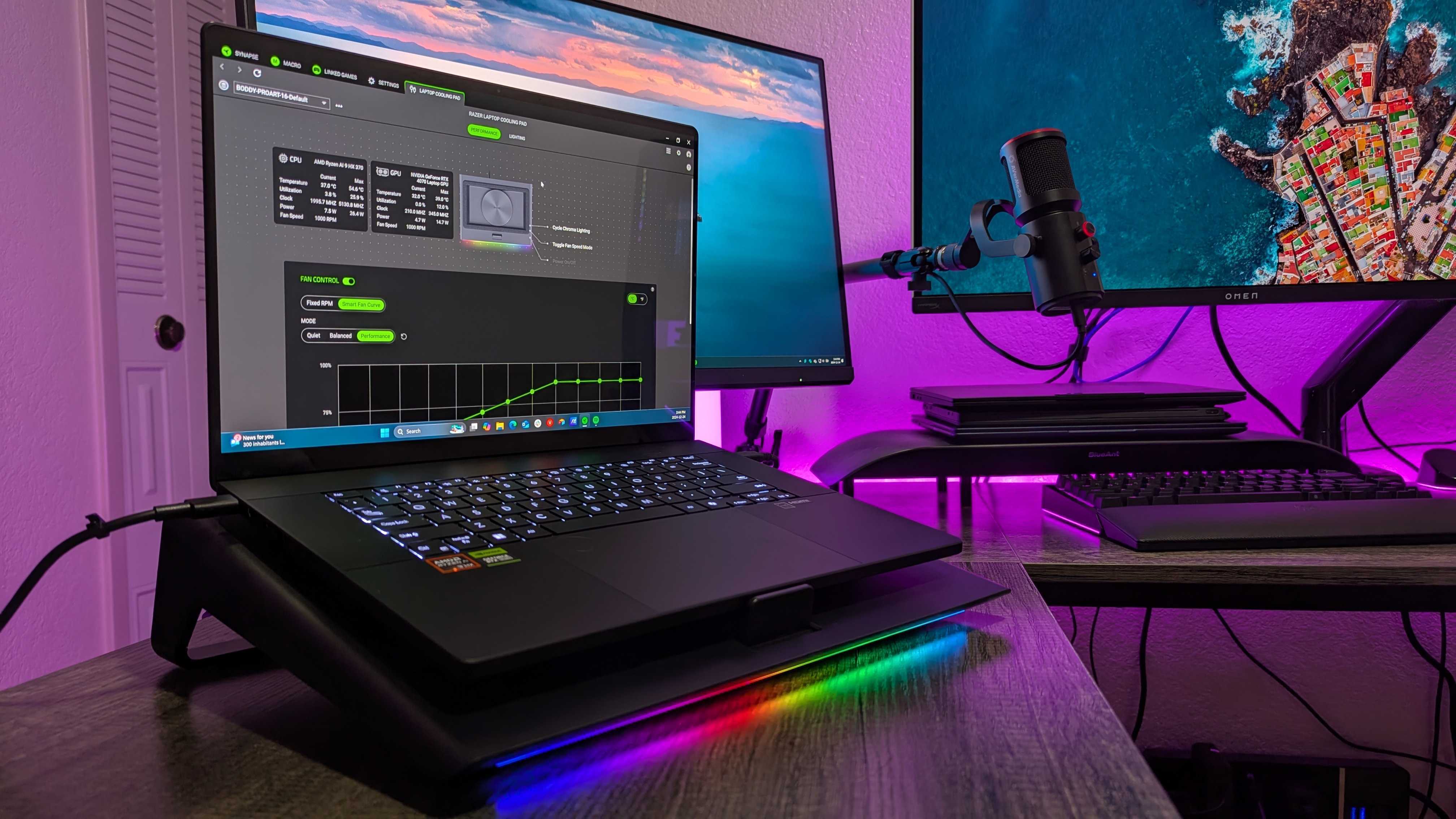Masanın üzerindeki Razer Dizüstü Bilgisayar Soğutma Pedi, ASUS ProArt P16 (2024) dizüstü bilgisayarın takılı ve RGB aydınlatmanın etkin olduğunu gösteriyor.