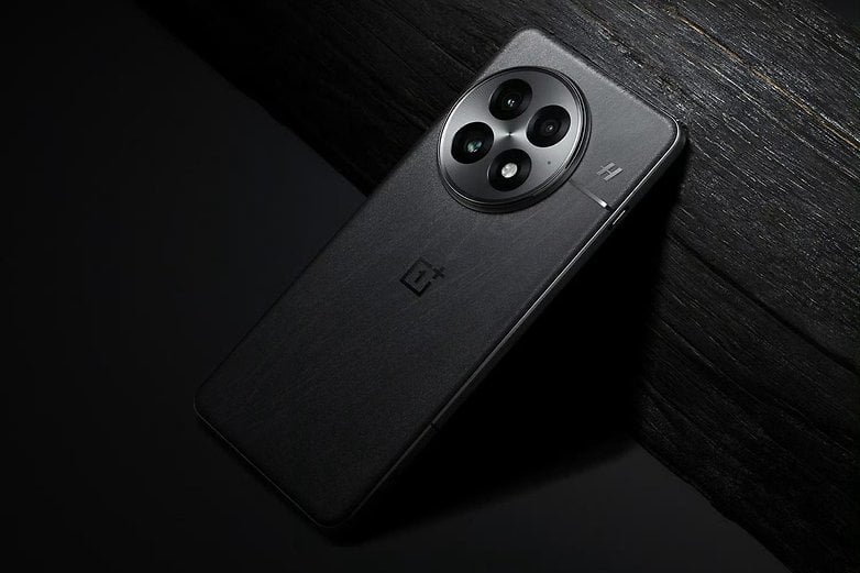 OnePlus 13 akıllı telefon, koyu renkli ahşap bir yüzeyin üzerinde yer alıyor ve ince tasarımını ve üçlü kamera kurulumunu sergiliyor.