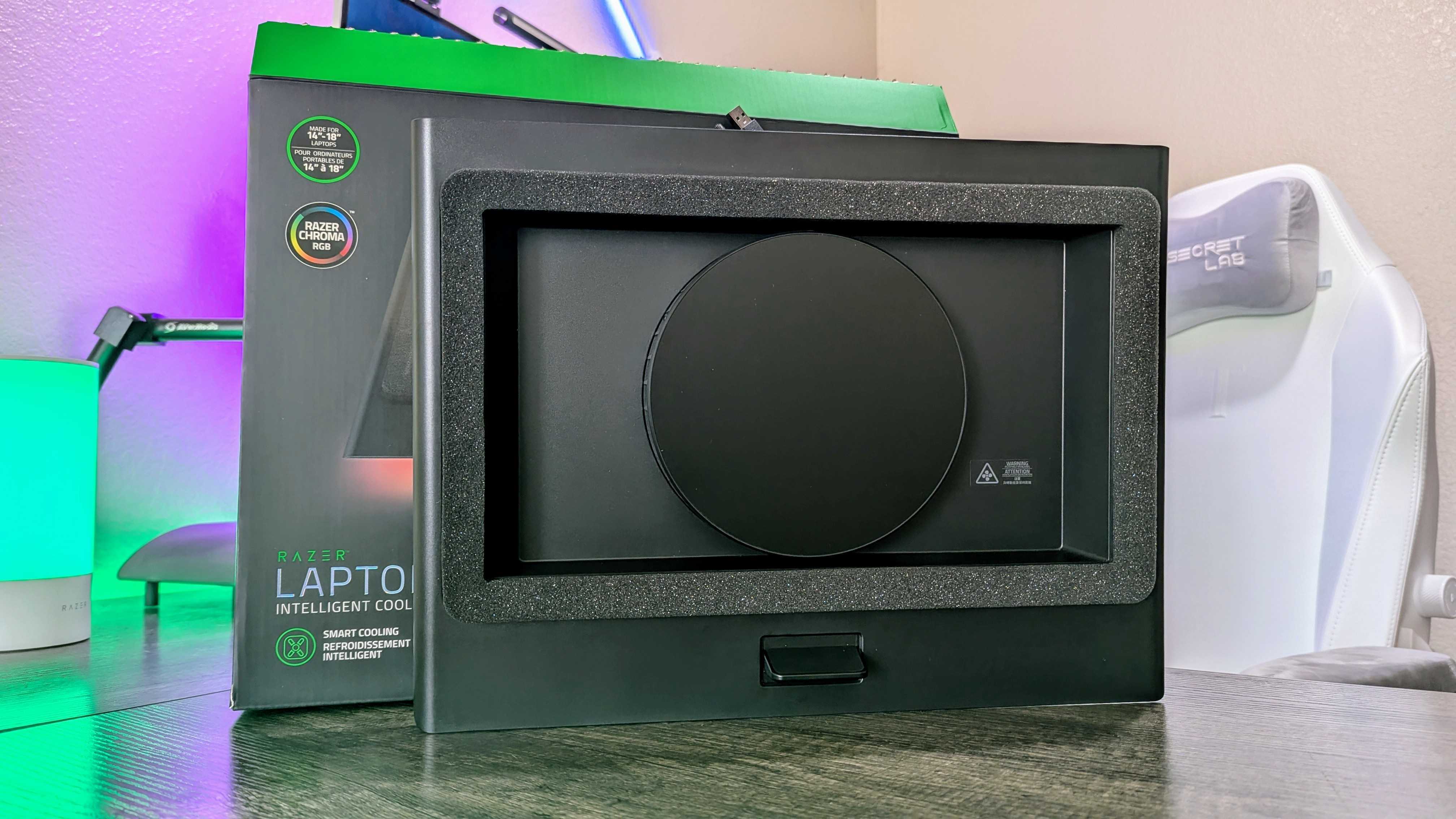 Razer Dizüstü Bilgisayar Soğutma Pedi, ambalajının üzerinde dikey olarak desteklenmiş olarak masanın üzerinde duruyor.