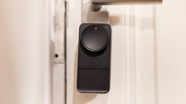 Yuvarlak düğmeli ve gösterge ışıklı bir kapıya monte edilmiş siyah SwitchBot Lock Pro.
