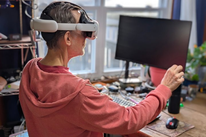 Alan Truly bir Windows PC'nin önünde oturuyor ve Meta Quest 3 VR kulaklığı takarken sanal ekranı ayarlıyor.
