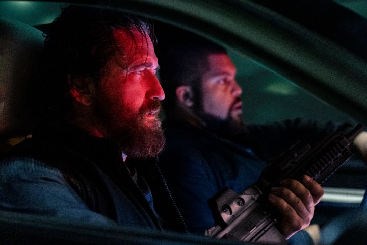 Gerard Butler bir arabanın ön koltuğunda otururken elinde silah tutuyor.