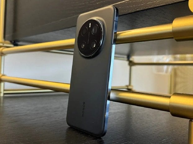 Siyah bir Honor Magic 7 Pro akıllı telefon, altın renkli bir rafa yaslanıyor.