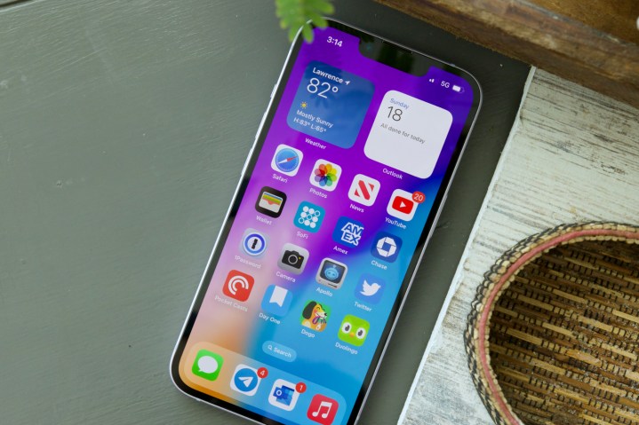 Bir masaya döşenen bir iPhone 14. Ekran açık ve ana ekranı gösteriyor.