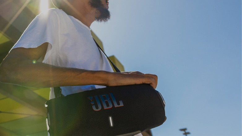 Beyaz tişörtlü bir kişi JBL Xtreme 4 taşınabilir hoparlörü tutuyor.