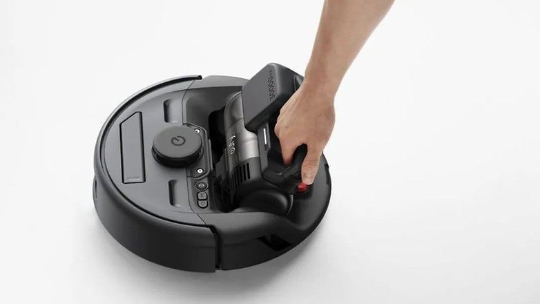 Bir kişi beyaz yüzeydeki robot elektrikli süpürgeden el tipi elektrikli süpürgeyi çıkarıyor.
