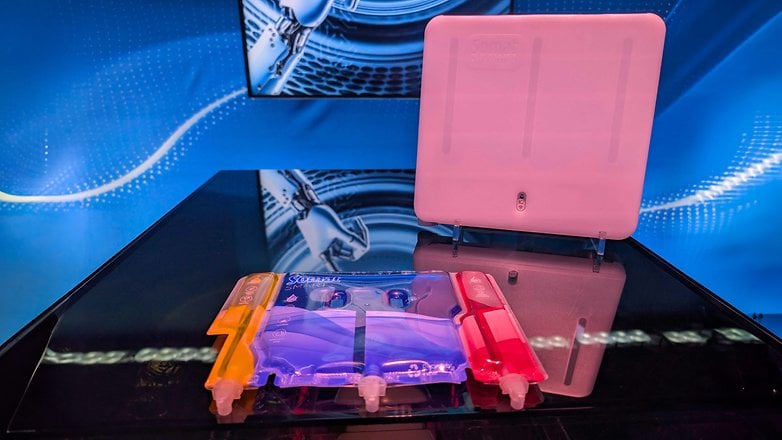 CES 2025'teki bir masada dijital arka planda görüntülenen, renkli bölümlere sahip şeffaf bir cihaz. CES 2025'teki bir masada dijital arka planda görüntülenen, renkli bölümlere sahip şeffaf bir cihaz.