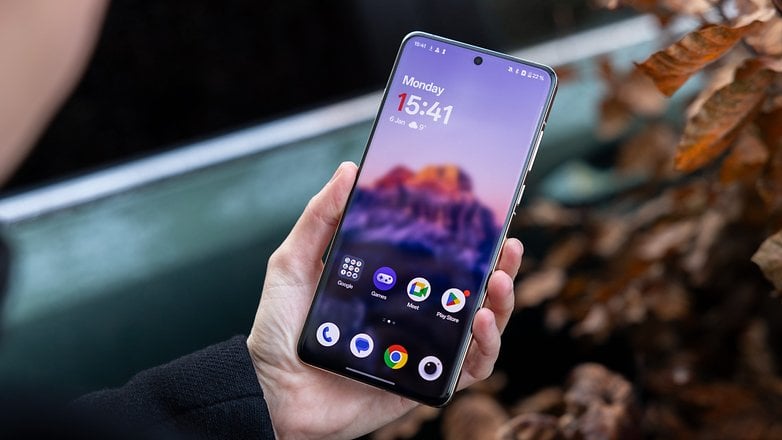 Bir kişi, ana ekranı saat ve uygulamalarla gösteren OnePlus 13 akıllı telefonunu tutuyor. Bir kişi, ana ekranı saat ve uygulamalarla gösteren OnePlus 13 akıllı telefonunu tutuyor.