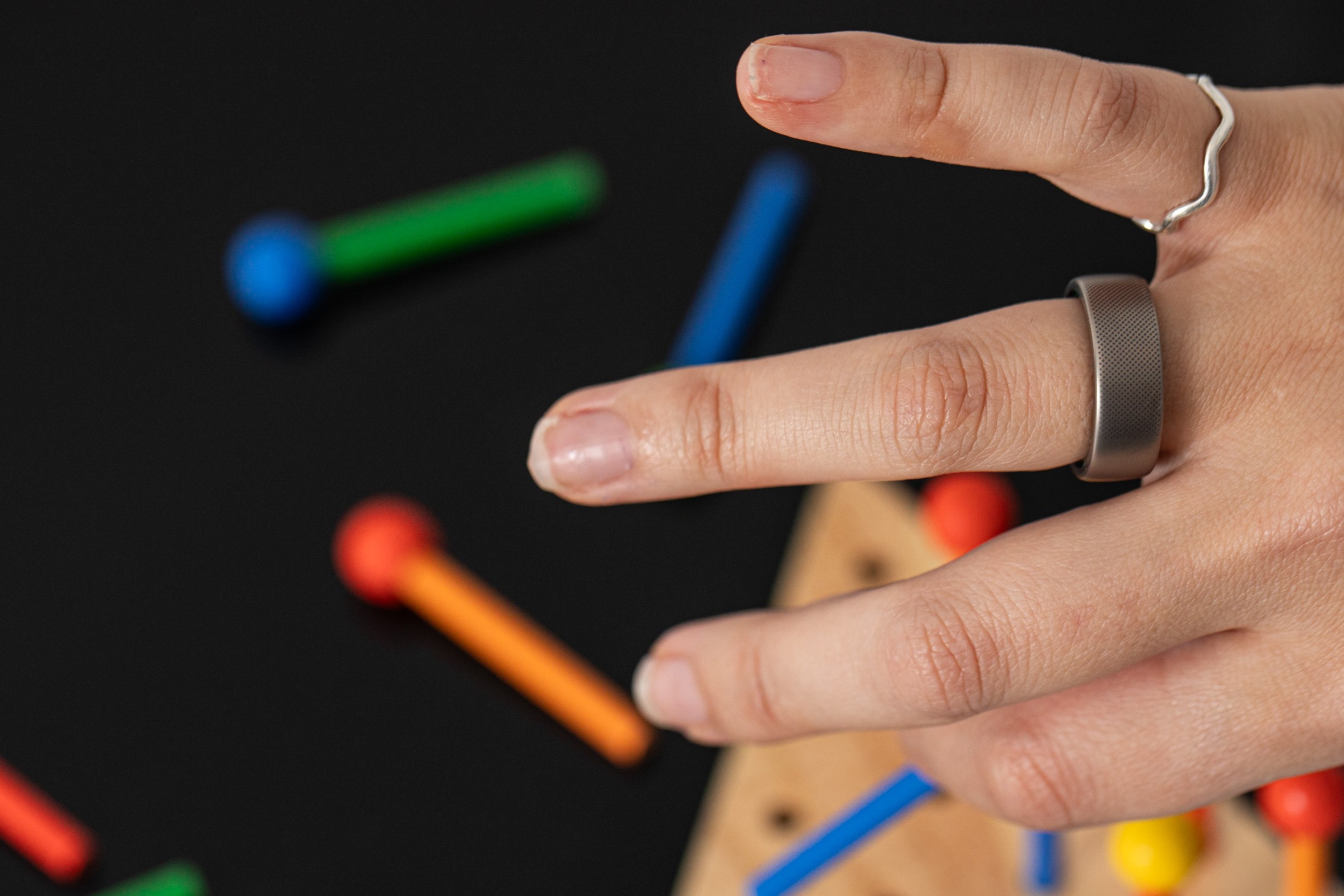 Arka planda renkli ahşap oyuncak ile Amazfit helio ring giyen kişi