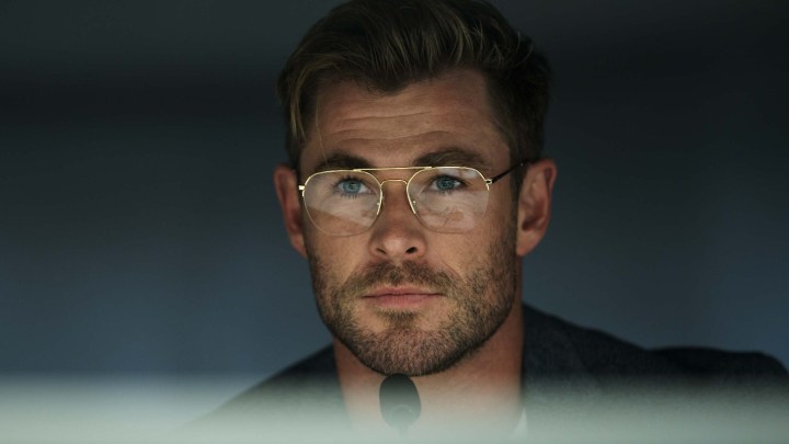 Chris Hemsworth, Spiderhead'den bir sahnede Mi Crofon'un önünde sırıtıyor.