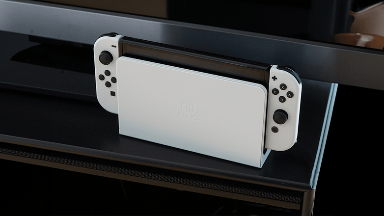Siyah bir rafa yerleştirilmiş beyaz renkte bir Nintendo anahtarı OLED konsolu.