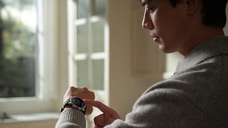 Bir kişi bir OnePlus Watch 3 giyer ve bir pencerede dururken ekranı kontrol eder.