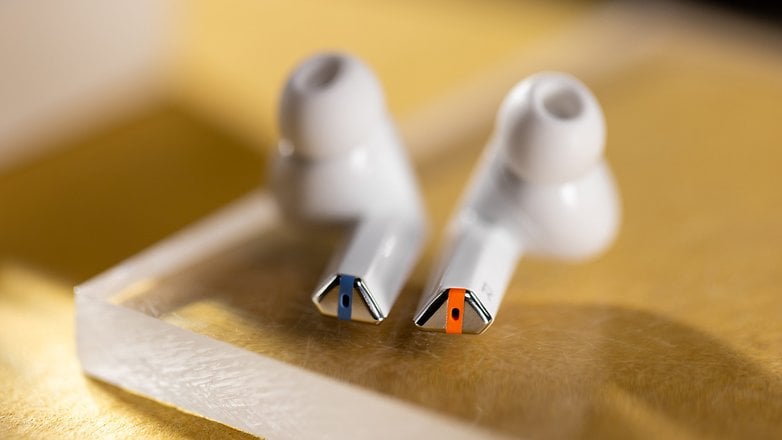 Yansıtıcı bir yüzeyde mavi ve turuncu aksanlarla Samsung Galaxy Buds 3 Pro'nun kapatılması.