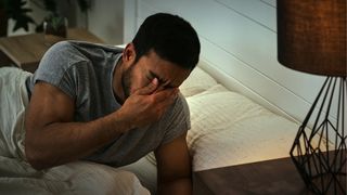Uyku felci ile uyurken elleri gözleri üzerinde yatağa yaslanan bir adam