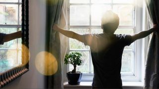 Pencere açılış perdesinde duran adam sabah ışığı içeri girmek için.
