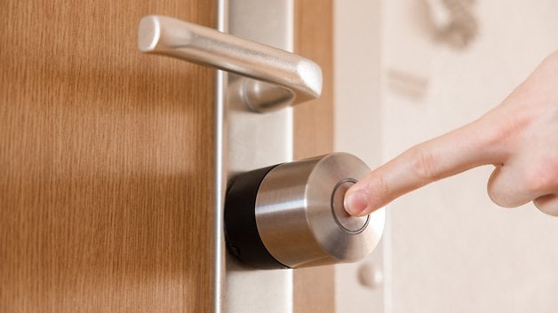 Bir el, ahşap bir kapıya bağlı bir Nuki Smart Lock Pro'nun düğmesine basar.