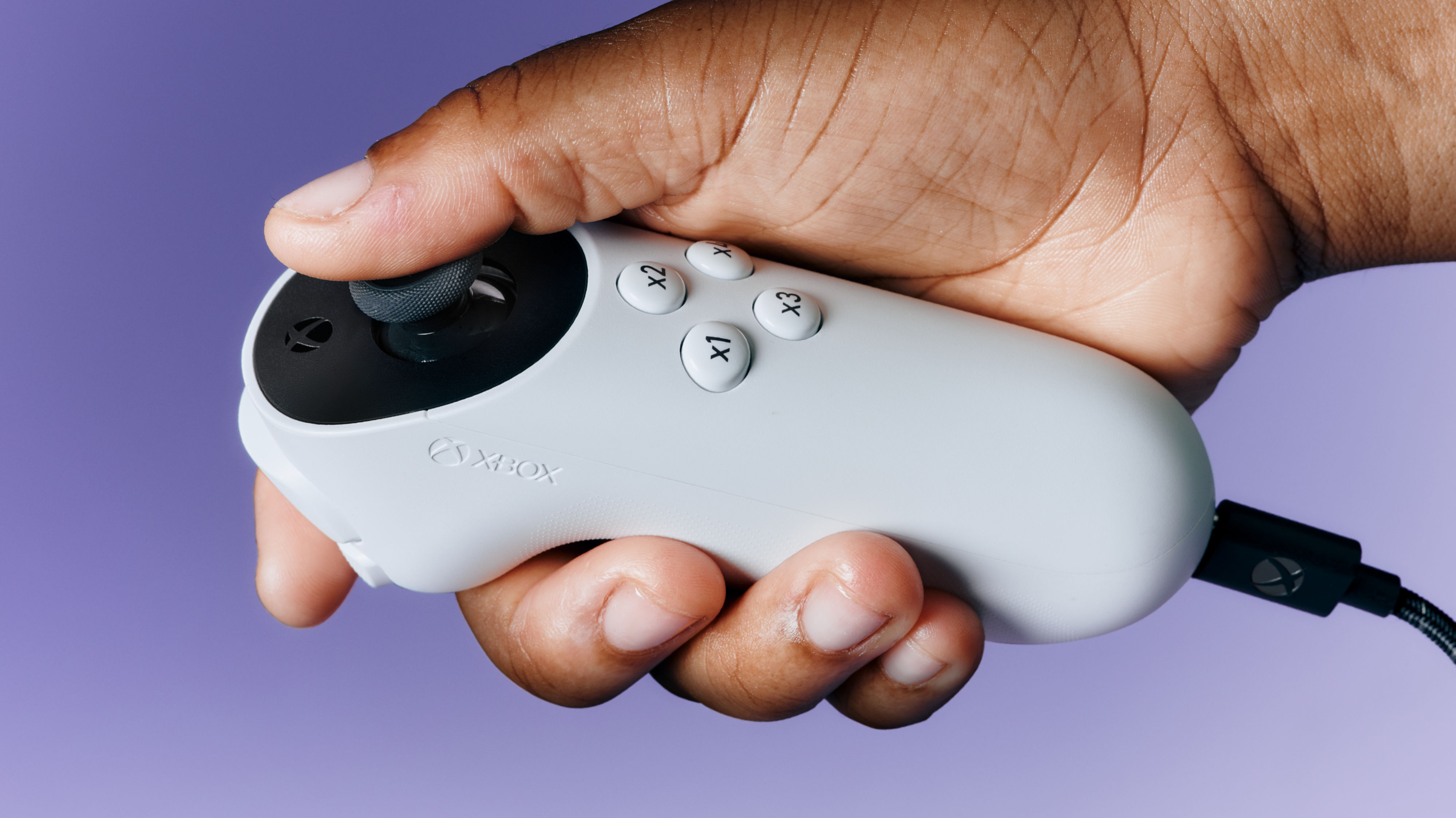 Tek bir el, Xbox uyarlamalı joystick'i mor arka planla tutar.