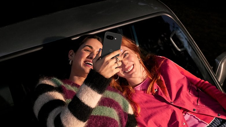 Bir arabada yatarken iki kadın güler ve bir Google Pixel 9A cep telefonuna bakar.