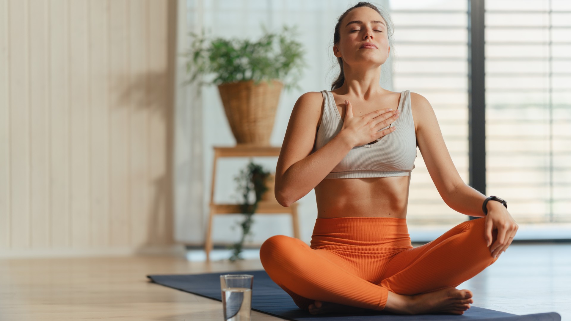 Hafif ve havadar stüdyo çapraz bacaklı bir solunum egzersizi gerçekleştiren yoga mat üzerinde oturan kadın
