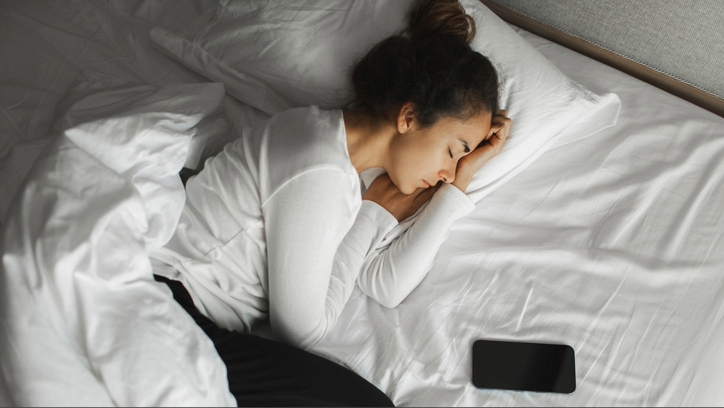 Yanında, telefonun yanında beyaz çarşaflarla yatakta beyaz üst giyen bir kadın