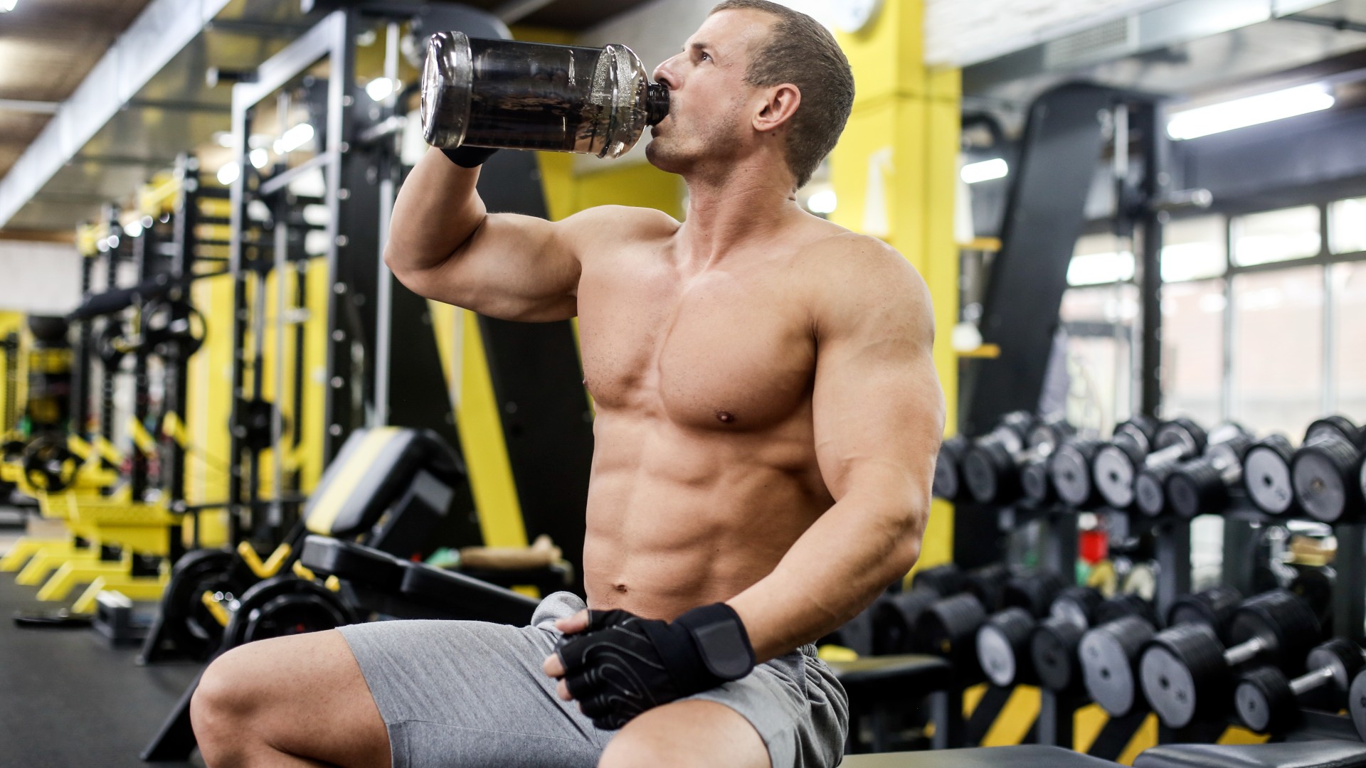 Direnç egzersizi sırasında protein çalkalayıcıdan içen bir egzersiz bankında oturan adam